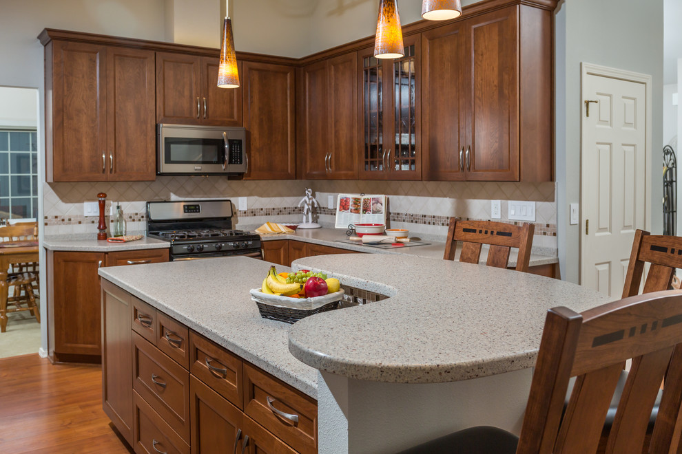Mid-sized transitional u-shaped medium tone wood floor kitchen pantry photo with an undermount sink, recessed-panel cabinets, medium tone wood cabinets, solid surface countertops, beige backsplash, mosaic tile backsplash, stainless steel appliances and an island