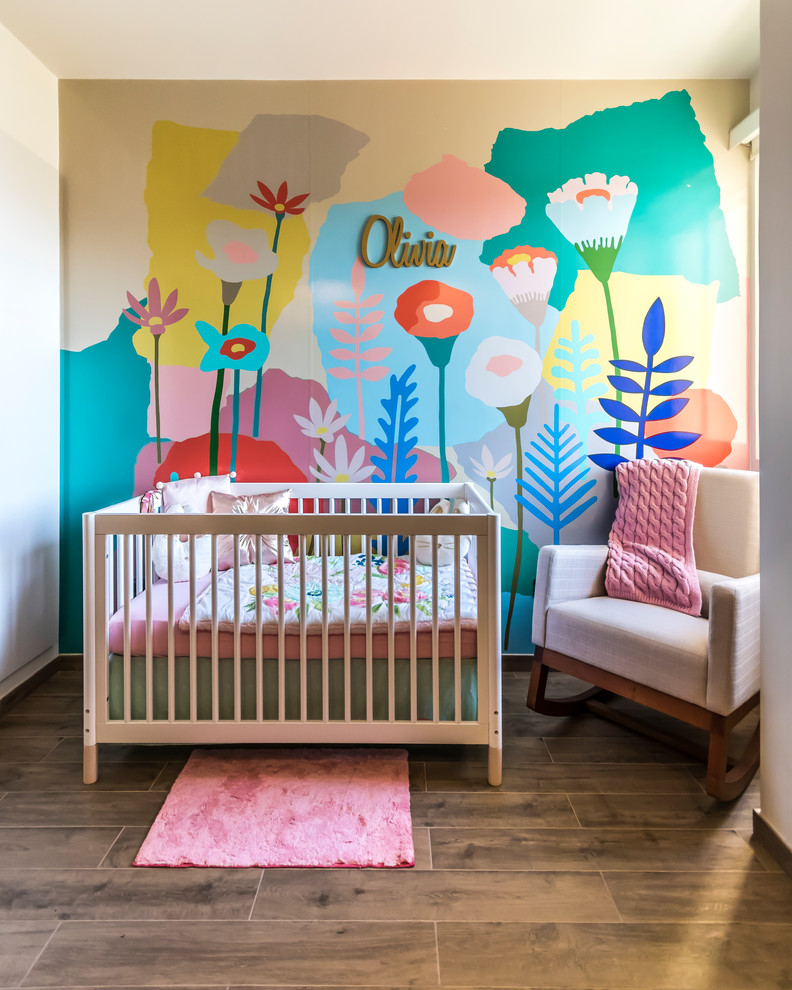 Photo of a contemporary nursery for girls in Other with multi-coloured walls and light hardwood floors.