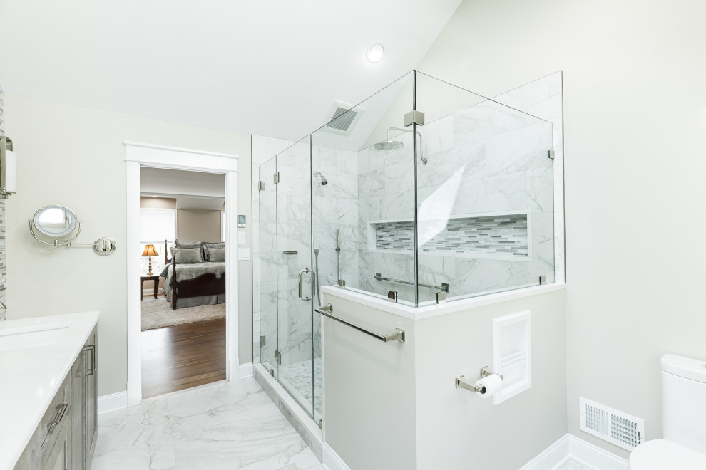 This is an example of a mid-sized transitional master bathroom in Philadelphia with recessed-panel cabinets, grey cabinets, a corner shower, a two-piece toilet, multi-coloured tile, glass tile, beige walls, porcelain floors, an undermount sink, engineered quartz benchtops, grey floor, a hinged shower door, white benchtops, a shower seat, a double vanity and a built-in vanity.