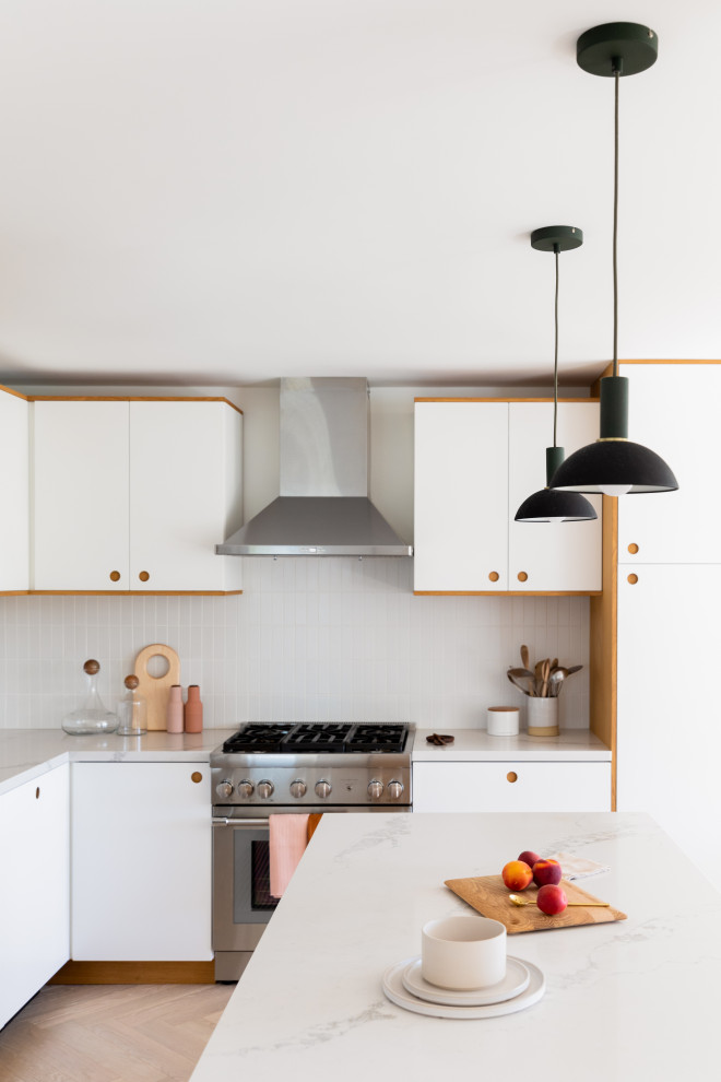 Small scandinavian l-shaped open plan kitchen in San Francisco with a submerged sink, flat-panel cabinets, light wood cabinets, engineered stone countertops, white splashback, ceramic splashback, stainless steel appliances, light hardwood flooring, an island, brown floors and white worktops.