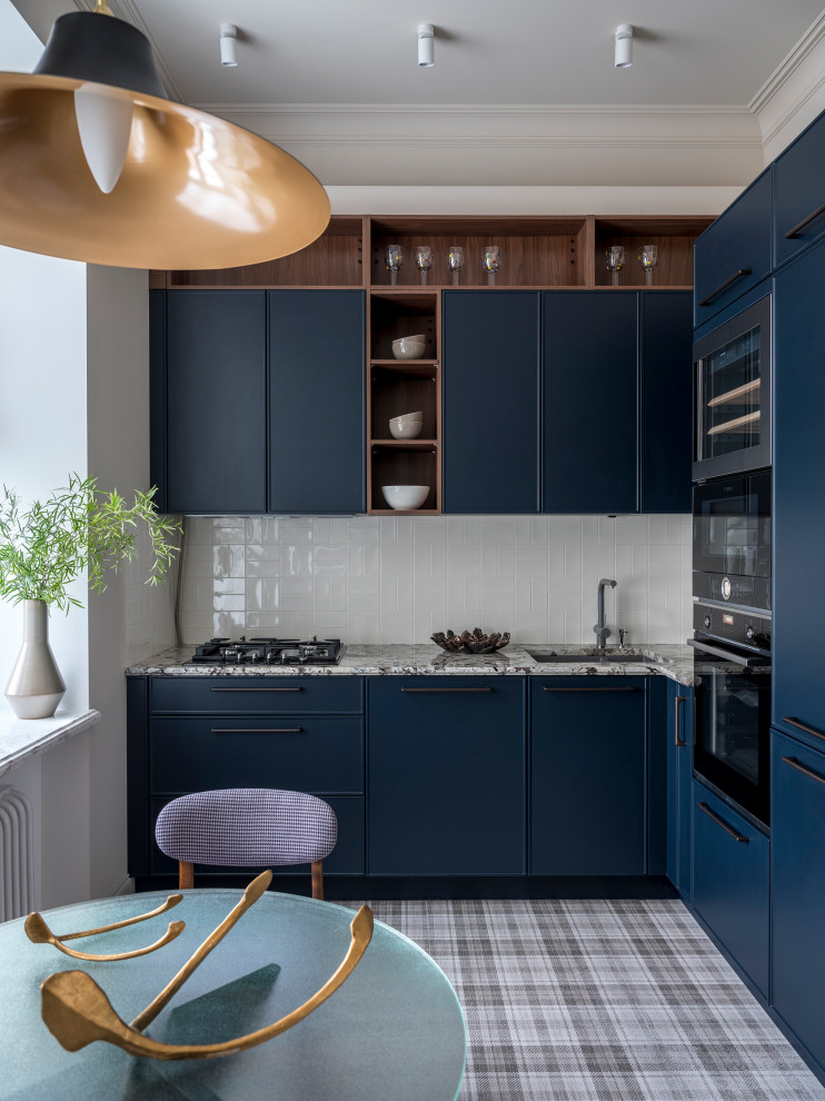 Transitional l-shaped eat-in kitchen in Moscow with an undermount sink, blue cabinets, white splashback, black appliances, no island, white benchtop, beaded inset cabinets and grey floor.