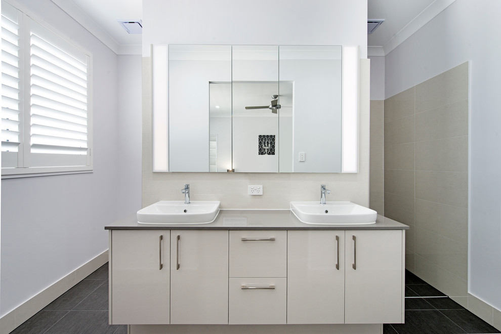 Photo of a mid-sized contemporary bathroom in Brisbane with flat-panel cabinets, white cabinets, beige tile, white walls, a vessel sink, black floor, ceramic tile, limestone benchtops and white benchtops.