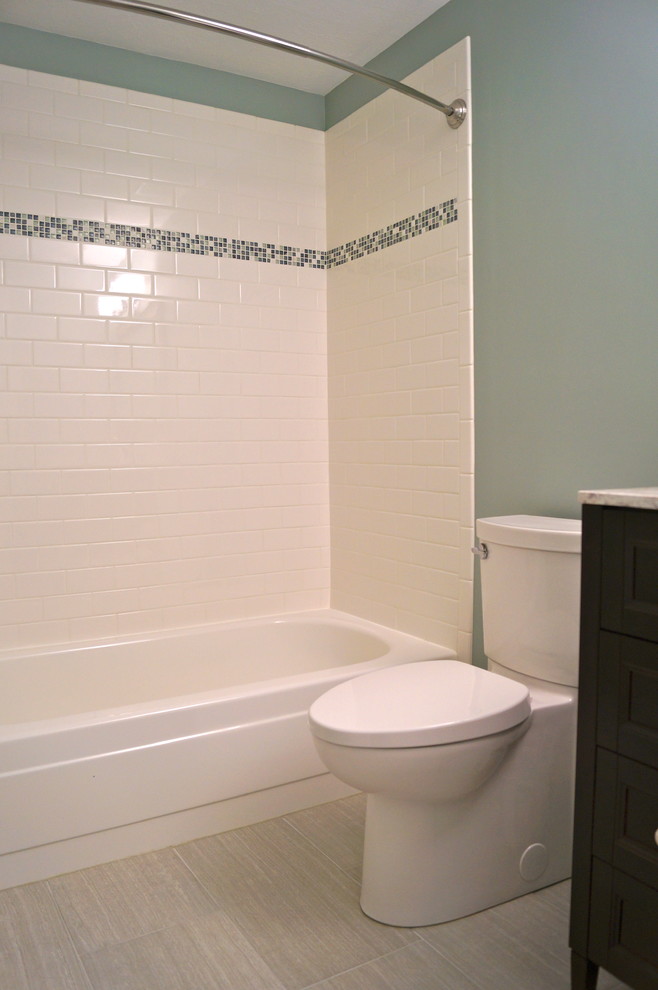 This is an example of a small modern bathroom in Cleveland with shaker cabinets, dark wood cabinets, solid surface benchtops, a drop-in tub, a one-piece toilet, white tile, ceramic tile, blue walls and porcelain floors.