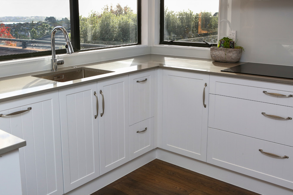Inspiration for a mid-sized country u-shaped open plan kitchen in Auckland with an undermount sink, shaker cabinets, white cabinets, quartz benchtops, grey splashback, glass sheet splashback, stainless steel appliances, medium hardwood floors, a peninsula, multi-coloured floor and grey benchtop.