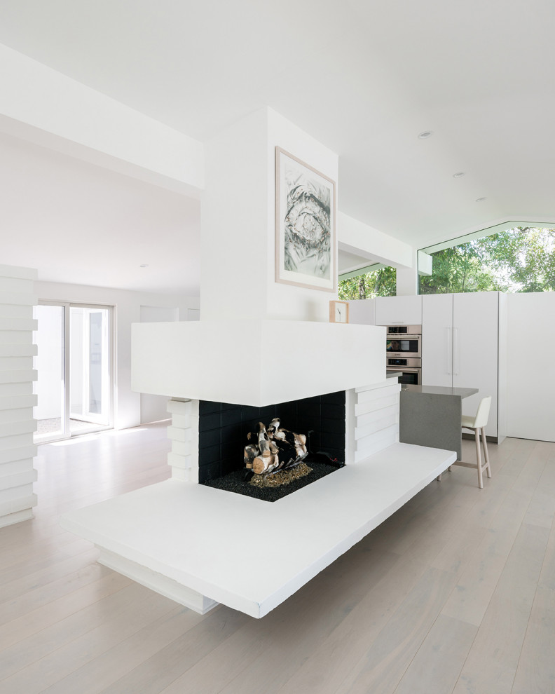 ロサンゼルスにある高級な中くらいなミッドセンチュリースタイルのおしゃれなLDK (白い壁、淡色無垢フローリング、標準型暖炉、コンクリートの暖炉まわり、白い床、表し梁) の写真