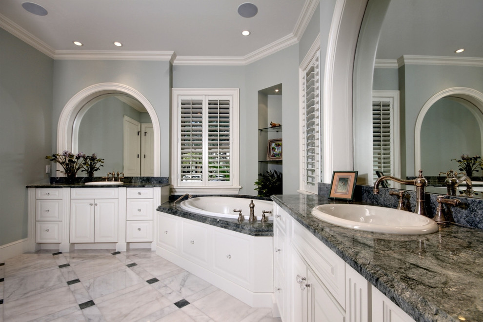 Design ideas for a large traditional master bathroom in Miami with raised-panel cabinets, white cabinets, a corner tub, a two-piece toilet, grey walls, marble floors, a drop-in sink, granite benchtops and white floor.