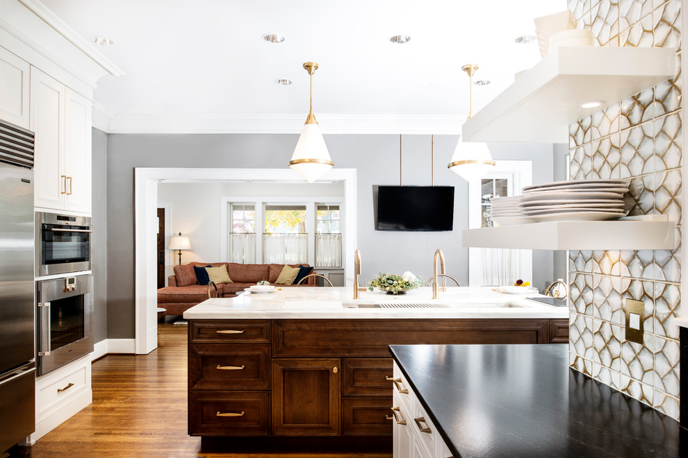 Inspiration for a large transitional u-shaped medium tone wood floor and brown floor eat-in kitchen remodel with white backsplash, glass tile backsplash, stainless steel appliances, an island, a farmhouse sink, recessed-panel cabinets, white cabinets and marble countertops