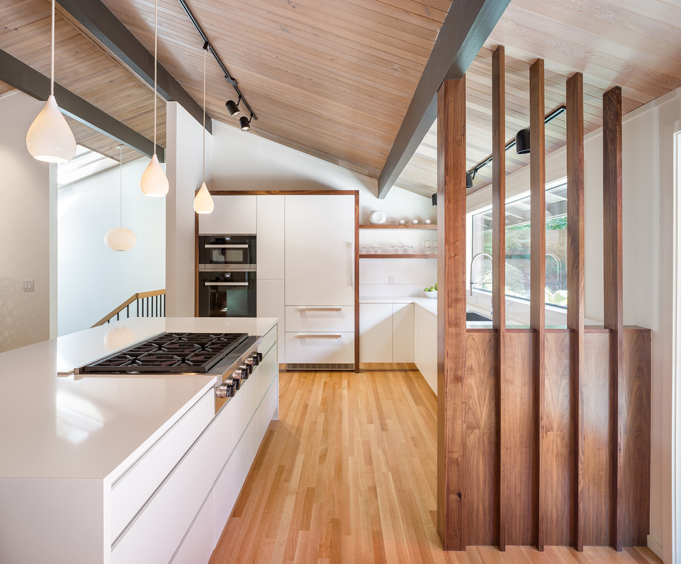 This is an example of a midcentury l-shaped kitchen in Portland with an undermount sink, flat-panel cabinets, white cabinets, stainless steel appliances, medium hardwood floors, with island and multi-coloured floor.