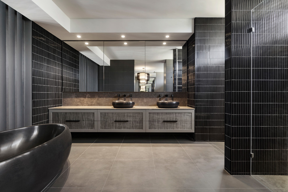 Design ideas for a contemporary master bathroom in Melbourne with flat-panel cabinets, grey cabinets, a freestanding tub, black tile, a vessel sink and a hinged shower door.