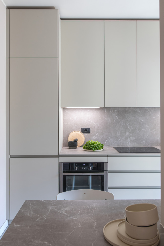 Small contemporary galley eat-in kitchen in Milan with an undermount sink, glass-front cabinets, beige cabinets, laminate benchtops, grey splashback, black appliances, porcelain floors, no island, grey floor and grey benchtop.