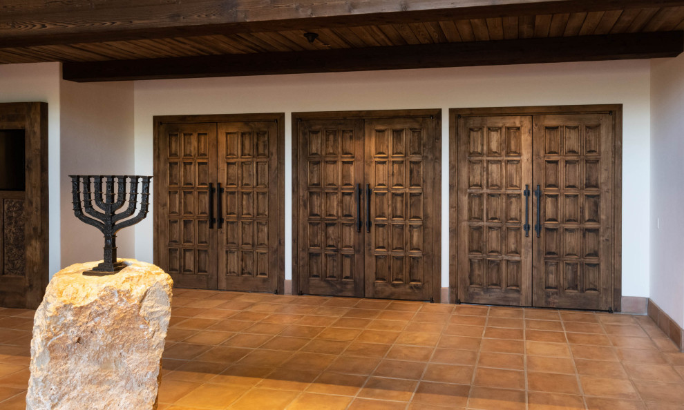 Aménagement d'une grande porte d'entrée classique avec un mur blanc, tomettes au sol, une porte double, une porte marron, un sol orange et poutres apparentes.