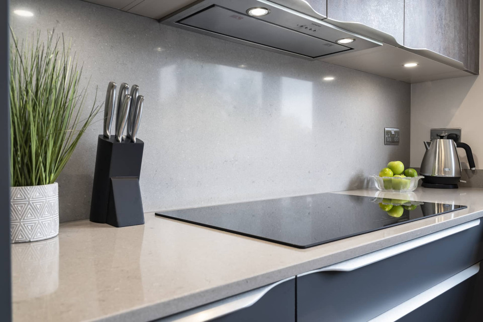 This is an example of a large modern l-shaped eat-in kitchen in Oxfordshire with flat-panel cabinets, quartzite benchtops, black appliances and with island.
