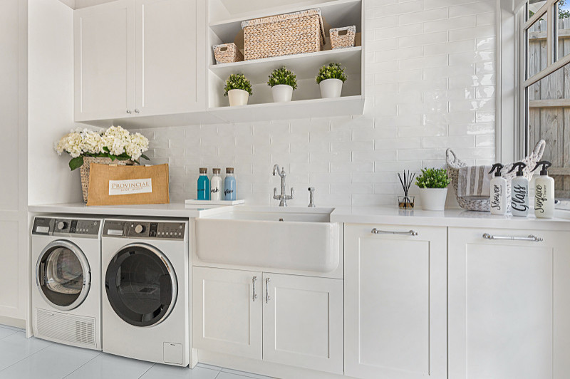 Design ideas for a mid-sized country single-wall dedicated laundry room in Melbourne with a farmhouse sink, shaker cabinets, white cabinets, quartz benchtops, white splashback, subway tile splashback, beige walls, ceramic floors, a side-by-side washer and dryer, white floor and white benchtop.