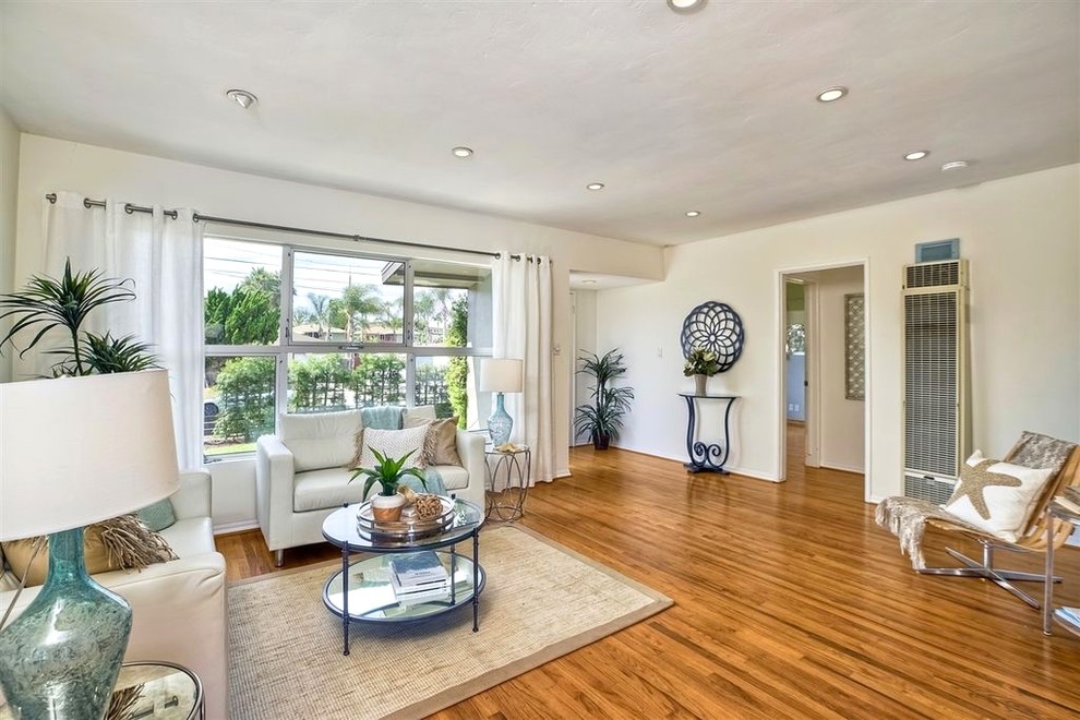 Photo of a mid-sized beach style open concept living room in San Diego with white walls, medium hardwood floors, no fireplace, a freestanding tv and brown floor.
