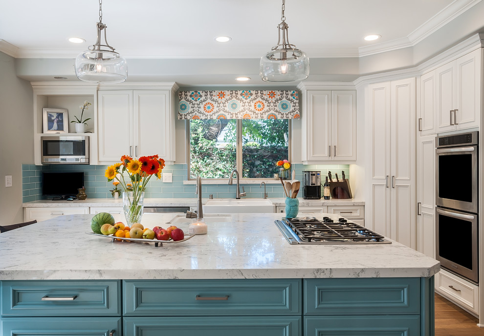Large beach style l-shaped open plan kitchen in Los Angeles with a farmhouse sink, beaded inset cabinets, white cabinets, quartz benchtops, blue splashback, glass tile splashback, stainless steel appliances, light hardwood floors, with island and multi-coloured floor.