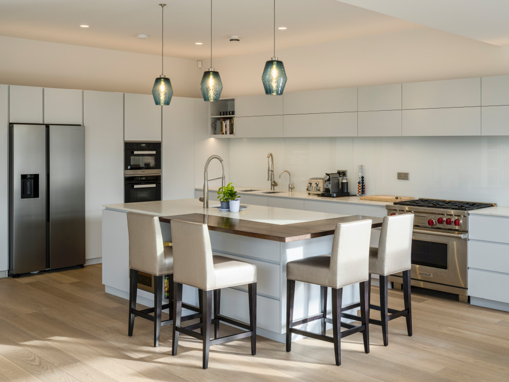 This is an example of a contemporary open plan kitchen in London with flat-panel cabinets, grey cabinets, white splashback, light hardwood flooring, an island and white worktops.