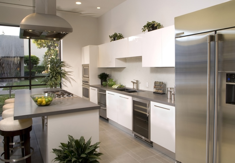 Design ideas for a large modern galley open plan kitchen in Toronto with an undermount sink, flat-panel cabinets, white cabinets, stainless steel benchtops, white splashback, glass tile splashback, stainless steel appliances, travertine floors, with island and beige floor.