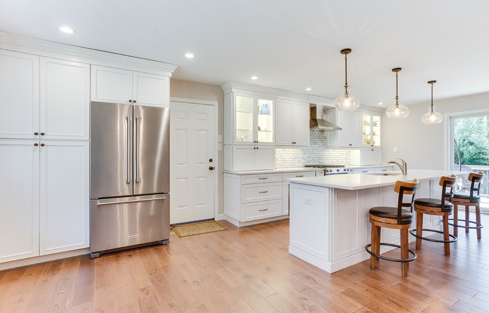 Large transitional galley medium tone wood floor and brown floor kitchen photo in DC Metro with an undermount sink, shaker cabinets, white cabinets, quartz countertops, gray backsplash, subway tile backsplash, stainless steel appliances and an island