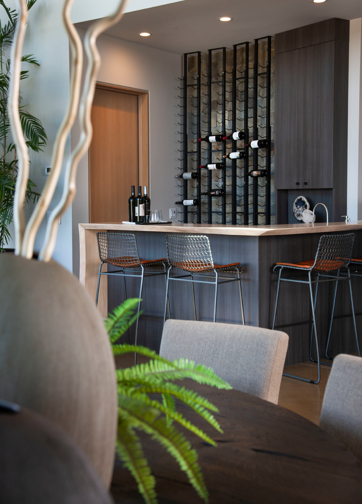 Photo of a large modern l-shaped seated home bar in San Diego with flat-panel cabinets, black cabinets, wood benchtops, concrete floors, grey floor and beige benchtop.