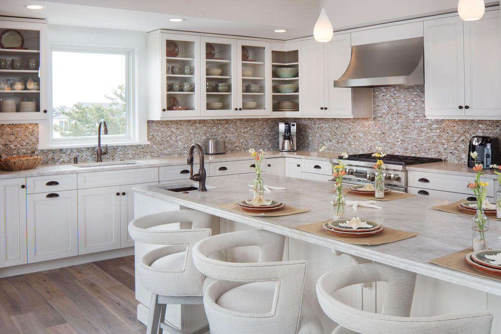 Large beach style l-shaped light wood floor and brown floor open concept kitchen photo with an undermount sink, recessed-panel cabinets, white cabinets, quartzite countertops, multicolored backsplash, stainless steel appliances, an island and mosaic tile backsplash