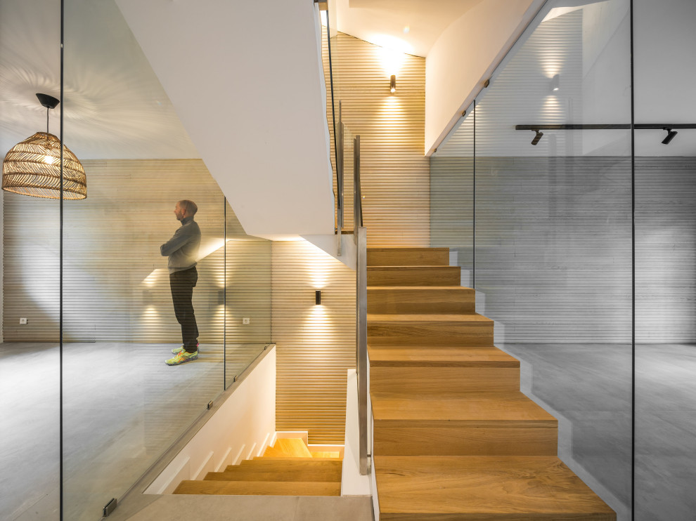 На фото: п-образная деревянная лестница среднего размера в стиле модернизм с деревянными ступенями, стеклянными перилами и стенами из вагонки