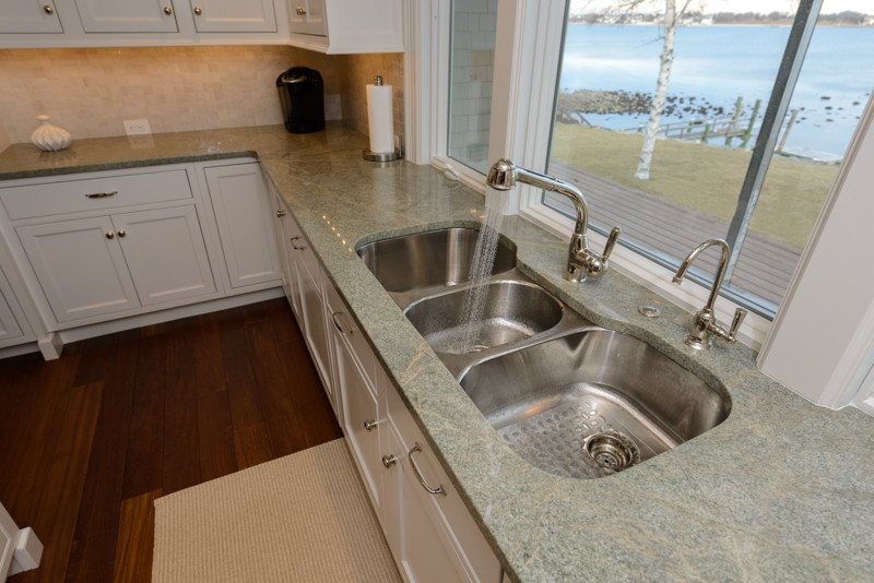 Example of a transitional medium tone wood floor kitchen design in Boston with a triple-bowl sink, recessed-panel cabinets, white cabinets, granite countertops, white backsplash, mosaic tile backsplash, stainless steel appliances and an island