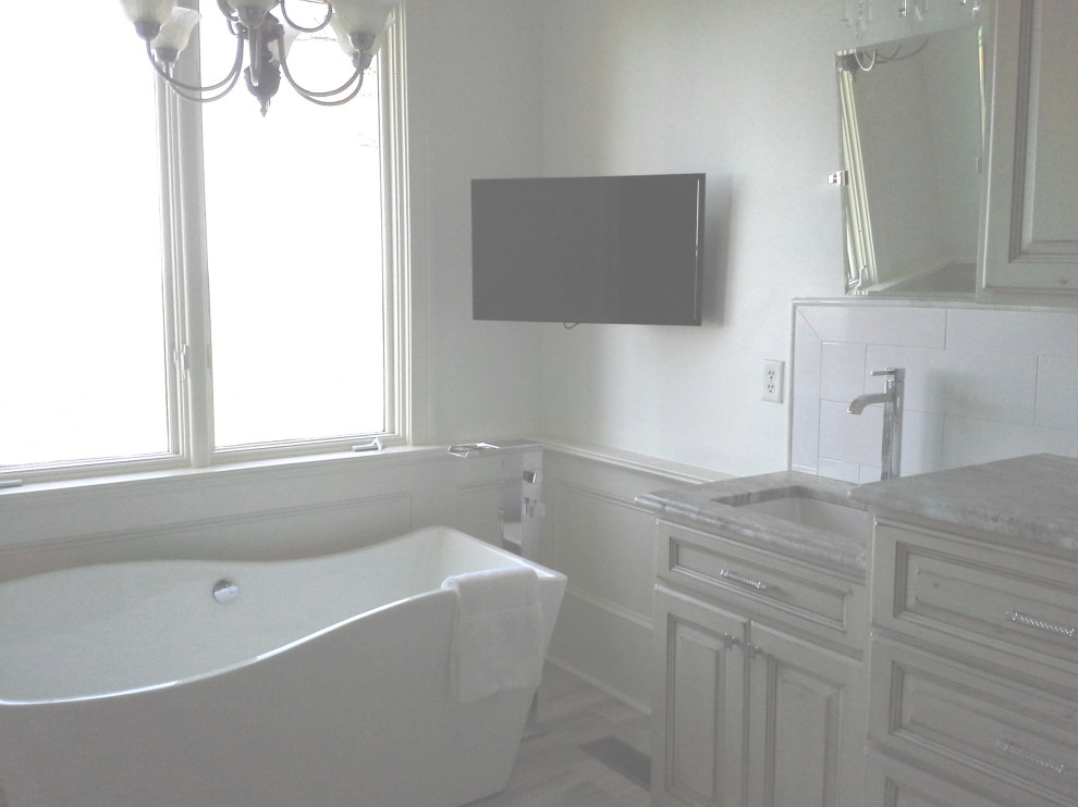 На фото: большая главная ванная комната в классическом стиле с фасадами с выступающей филенкой, серыми фасадами, отдельно стоящей ванной, душем в нише, раздельным унитазом, белой плиткой, керамогранитной плиткой, белыми стенами, полом из известняка, врезной раковиной, столешницей из гранита, серым полом, душем с распашными дверями, серой столешницей, тумбой под две раковины, напольной тумбой и панелями на стенах с
