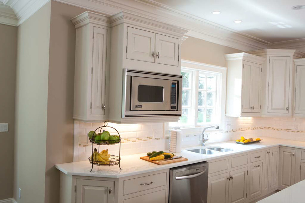 Large transitional l-shaped dark wood floor and brown floor eat-in kitchen photo with a drop-in sink, raised-panel cabinets, white cabinets, solid surface countertops, white backsplash, ceramic backsplash, stainless steel appliances and an island