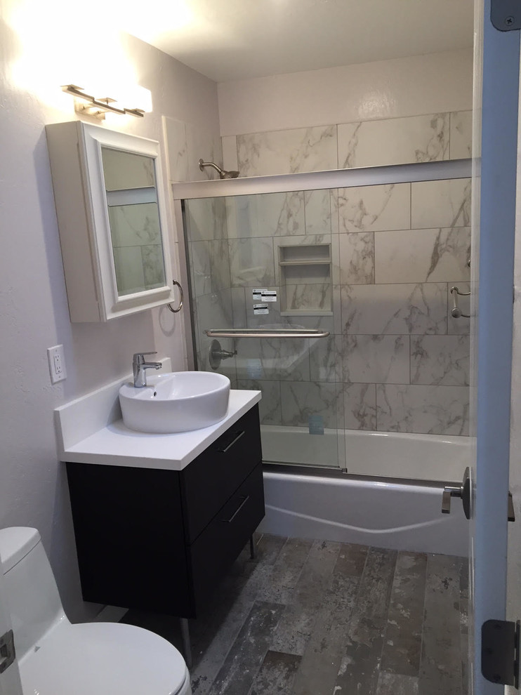 Mid-sized transitional bathroom in San Francisco with flat-panel cabinets, dark wood cabinets, an alcove tub, a shower/bathtub combo, a one-piece toilet, black and white tile, gray tile, marble, white walls, a vessel sink, solid surface benchtops and a sliding shower screen.