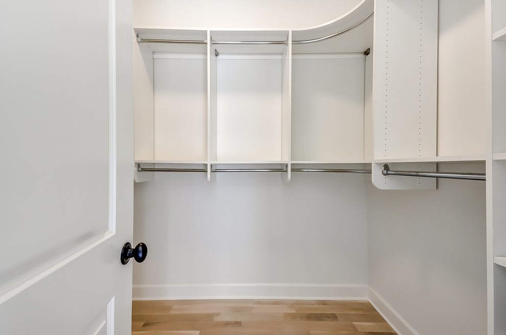 This is an example of a large country gender-neutral walk-in wardrobe in Atlanta with open cabinets, white cabinets, light hardwood floors and beige floor.