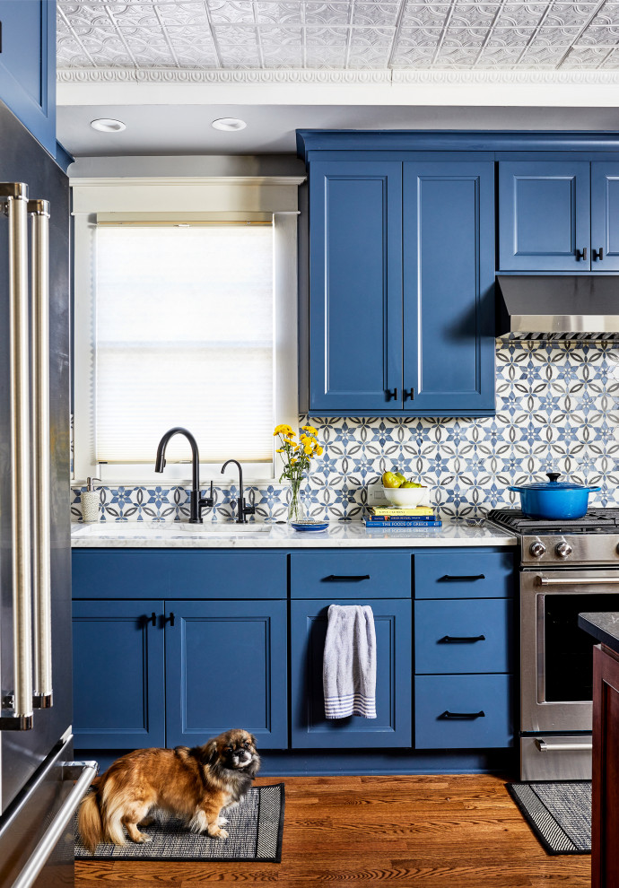 Exempel på ett mellanstort klassiskt kök och matrum, med blå skåp, blått stänkskydd, rostfria vitvaror, mellanmörkt trägolv och en köksö