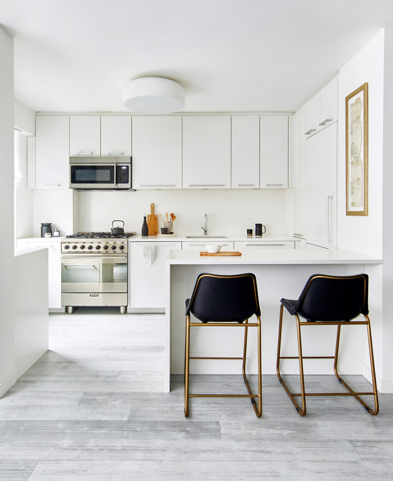 Inspiration for a mid-sized contemporary galley eat-in kitchen in New York with flat-panel cabinets, white cabinets, solid surface benchtops, white splashback, stainless steel appliances, grey floor, an undermount sink, a peninsula, glass sheet splashback, vinyl floors and white benchtop.