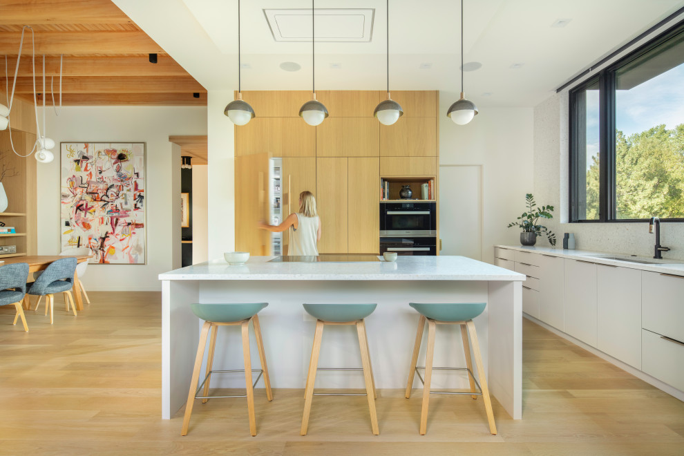 Example of a mid-century modern l-shaped light wood floor and wood ceiling open concept kitchen design in Denver with an undermount sink, flat-panel cabinets, light wood cabinets, terrazzo countertops, white backsplash, paneled appliances, an island and white countertops