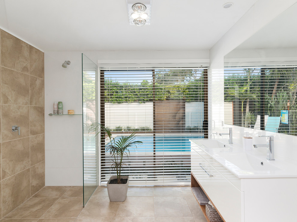 This is an example of a beach style bathroom in Gold Coast - Tweed with flat-panel cabinets, white cabinets, an open shower, beige tile, white walls, an integrated sink, beige floor, an open shower and white benchtops.