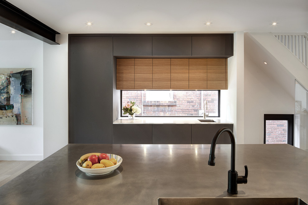 Photo of a small modern galley eat-in kitchen in Toronto with an integrated sink, flat-panel cabinets, grey cabinets, stainless steel benchtops, window splashback, black appliances, light hardwood floors and with island.