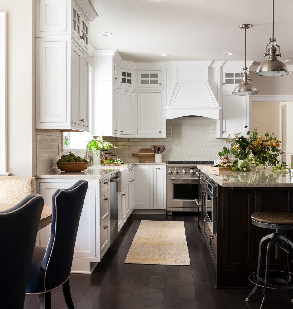 Inspiration for a large arts and crafts u-shaped open plan kitchen in Seattle with a farmhouse sink, beaded inset cabinets, white cabinets, quartzite benchtops, white splashback, ceramic splashback, stainless steel appliances, dark hardwood floors, with island and brown floor.