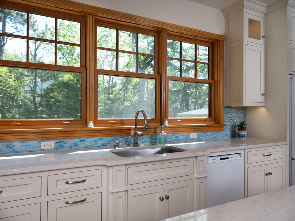 This is an example of a large traditional l-shaped open plan kitchen in Philadelphia with an undermount sink, flat-panel cabinets, white cabinets, blue splashback, glass tile splashback, white appliances, light hardwood floors, with island and blue floor.