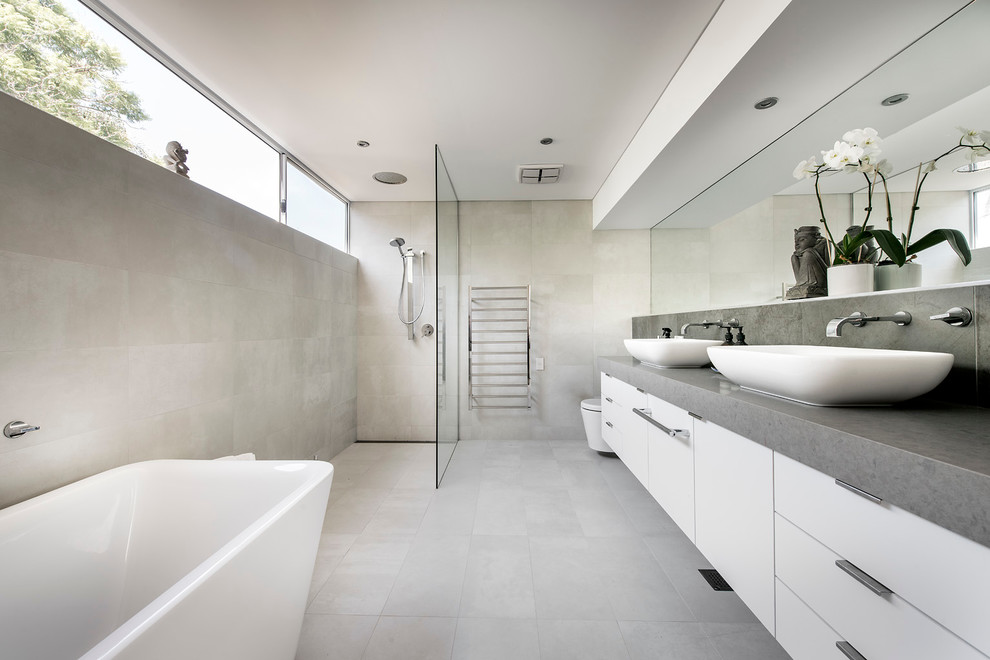 This is an example of a large contemporary master bathroom in Perth with flat-panel cabinets, white cabinets, a freestanding tub, an open shower, a wall-mount toilet, a vessel sink, an open shower and grey benchtops.