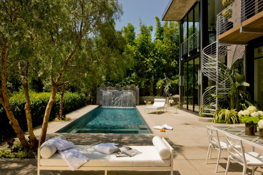 This is an example of a mid-sized contemporary backyard rectangular pool in Los Angeles with a water feature and concrete slab.