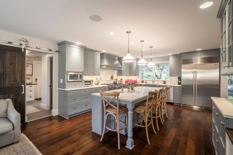 Large traditional l-shaped open plan kitchen in Minneapolis with a farmhouse sink, flat-panel cabinets, grey cabinets, quartz benchtops, white splashback, ceramic splashback, stainless steel appliances, medium hardwood floors and with island.
