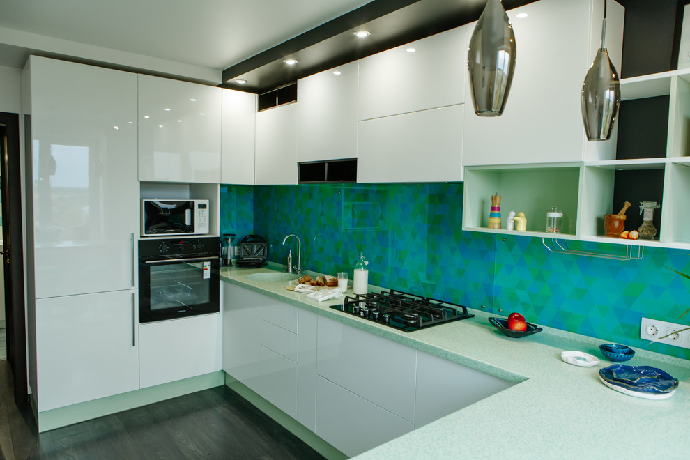 Design ideas for a mid-sized contemporary l-shaped separate kitchen in Other with an integrated sink, flat-panel cabinets, white cabinets, solid surface benchtops, green splashback, glass tile splashback, stainless steel appliances, laminate floors, no island, black floor and turquoise benchtop.