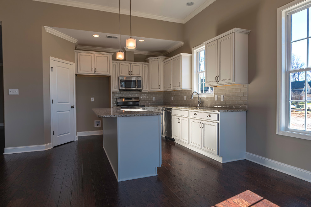 Mid-sized transitional l-shaped dark wood floor open concept kitchen photo with an undermount sink, white cabinets, granite countertops, gray backsplash, subway tile backsplash, stainless steel appliances, an island and recessed-panel cabinets