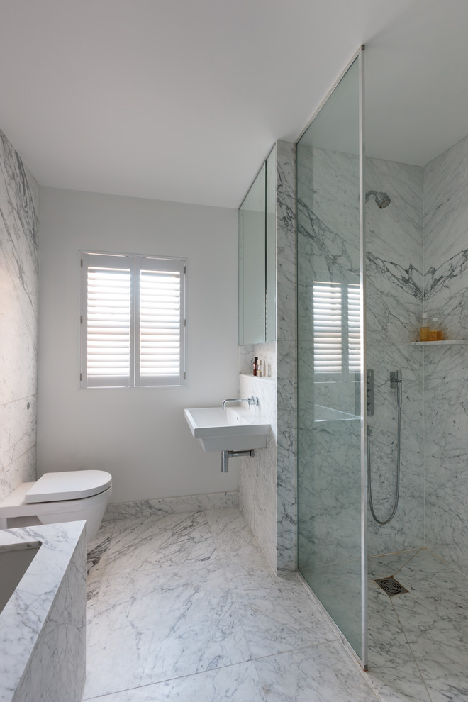 This is an example of a contemporary bathroom in London with marble floors, a wall-mount sink and marble.