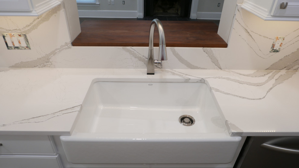 Example of a mid-sized transitional galley laminate floor and multicolored floor eat-in kitchen design with a farmhouse sink, shaker cabinets, white cabinets, quartz countertops, white backsplash, quartz backsplash, stainless steel appliances and white countertops