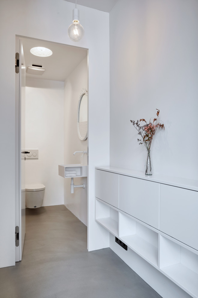 Modern inredning av ett stort vit vitt toalett, med luckor med lamellpanel, vita skåp, vita väggar, betonggolv och grått golv