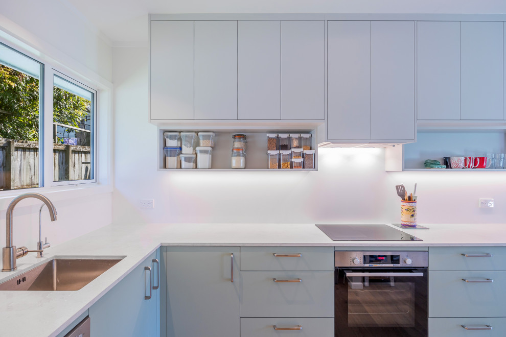 Example of a small trendy l-shaped laminate floor and brown floor eat-in kitchen design in Auckland with an undermount sink, flat-panel cabinets, green cabinets, quartz countertops, white backsplash, stainless steel appliances, no island and white countertops