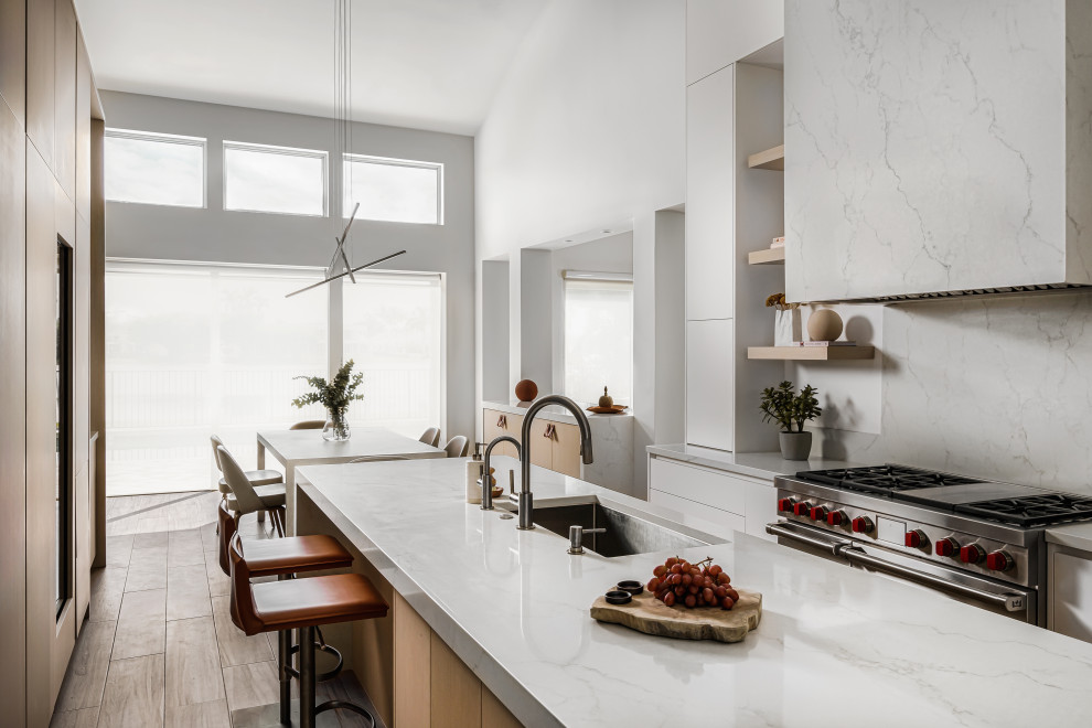 This is an example of a large scandinavian u-shaped eat-in kitchen in Miami with flat-panel cabinets, light wood cabinets, quartz benchtops, white splashback, engineered quartz splashback, stainless steel appliances, with island and white benchtop.