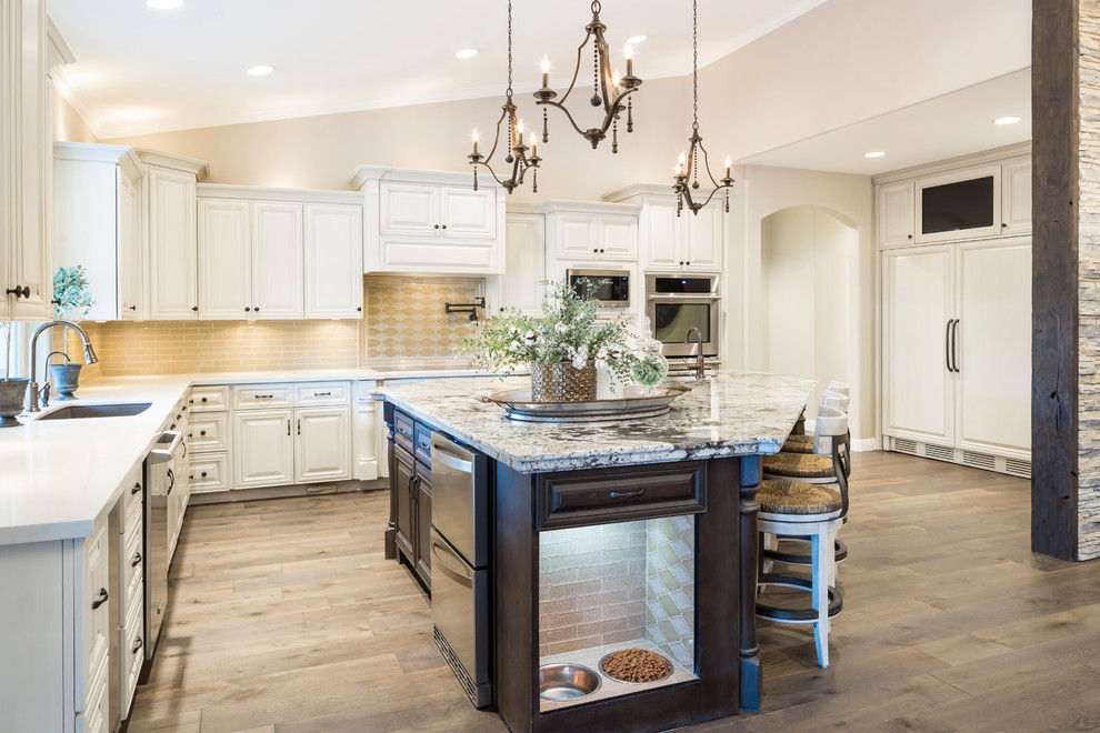 Eat-in kitchen - large transitional l-shaped medium tone wood floor and brown floor eat-in kitchen idea in Phoenix with an undermount sink, raised-panel cabinets, beige cabinets, quartz countertops, beige backsplash, glass tile backsplash, stainless steel appliances and an island