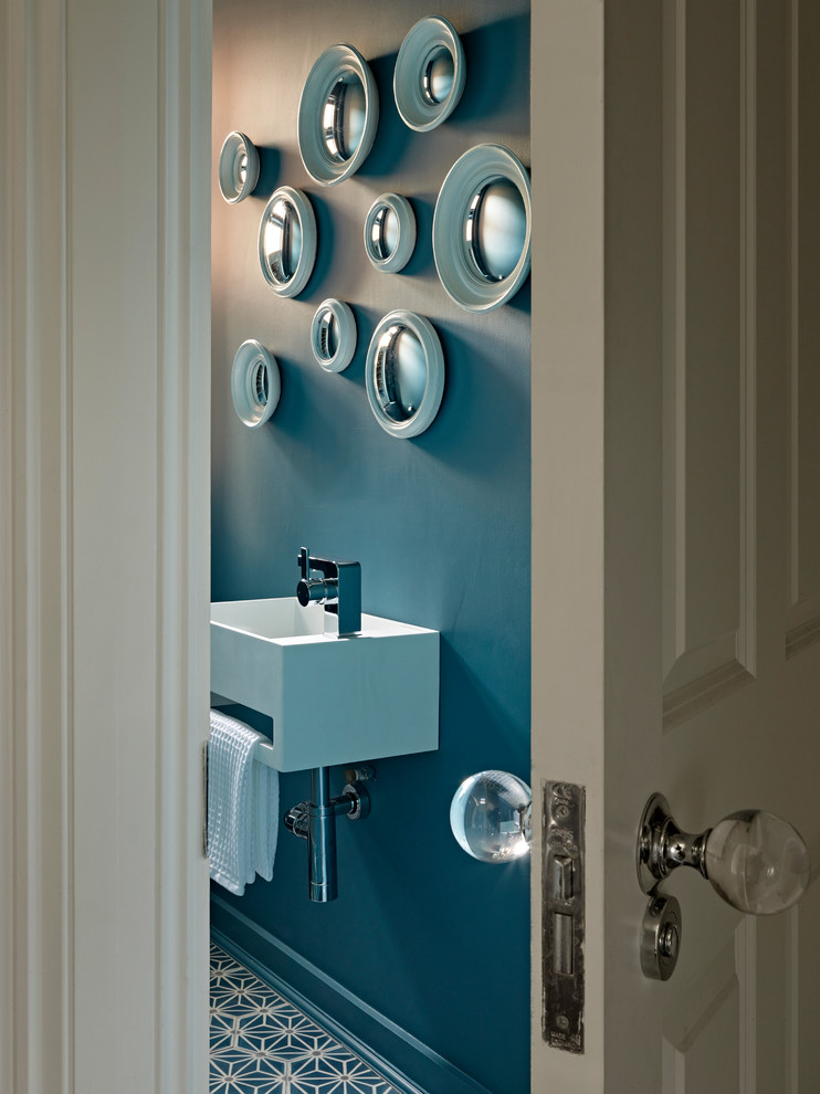 This is an example of a mid-sized contemporary powder room in London with a wall-mount toilet, a wall-mount sink, multi-coloured floor, blue walls and concrete floors.