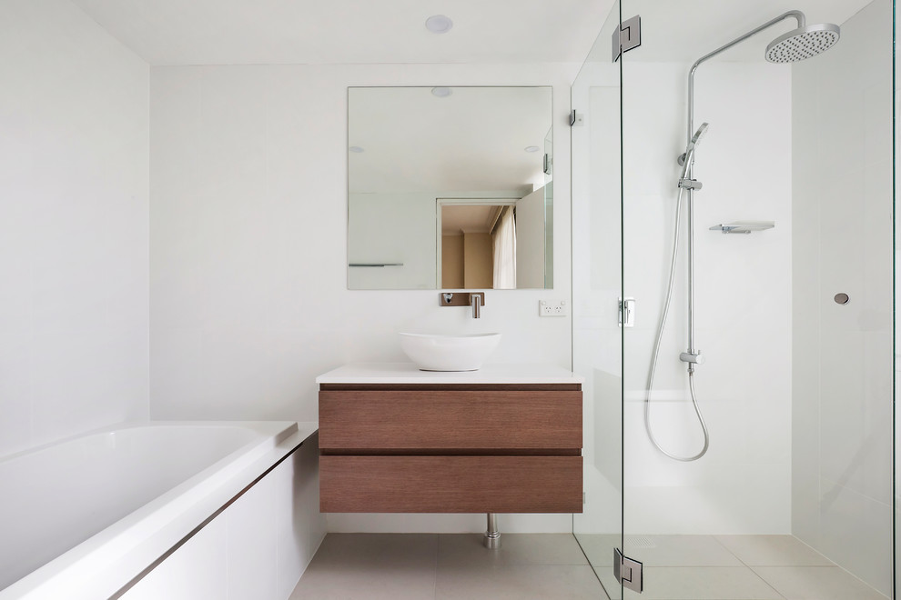Photo of a mid-sized contemporary master bathroom in Sydney with flat-panel cabinets, medium wood cabinets, a drop-in tub, a corner shower, a one-piece toilet, white tile, ceramic tile, white walls, porcelain floors, a vessel sink, engineered quartz benchtops, grey floor, a hinged shower door, white benchtops, a single vanity and a floating vanity.